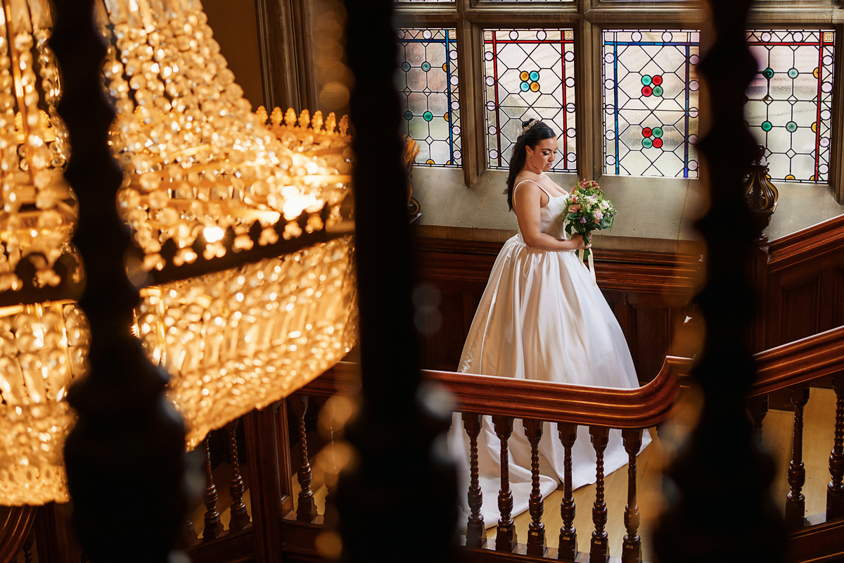 pendley manor wedding photographer - bride on stairs looking at bouquet