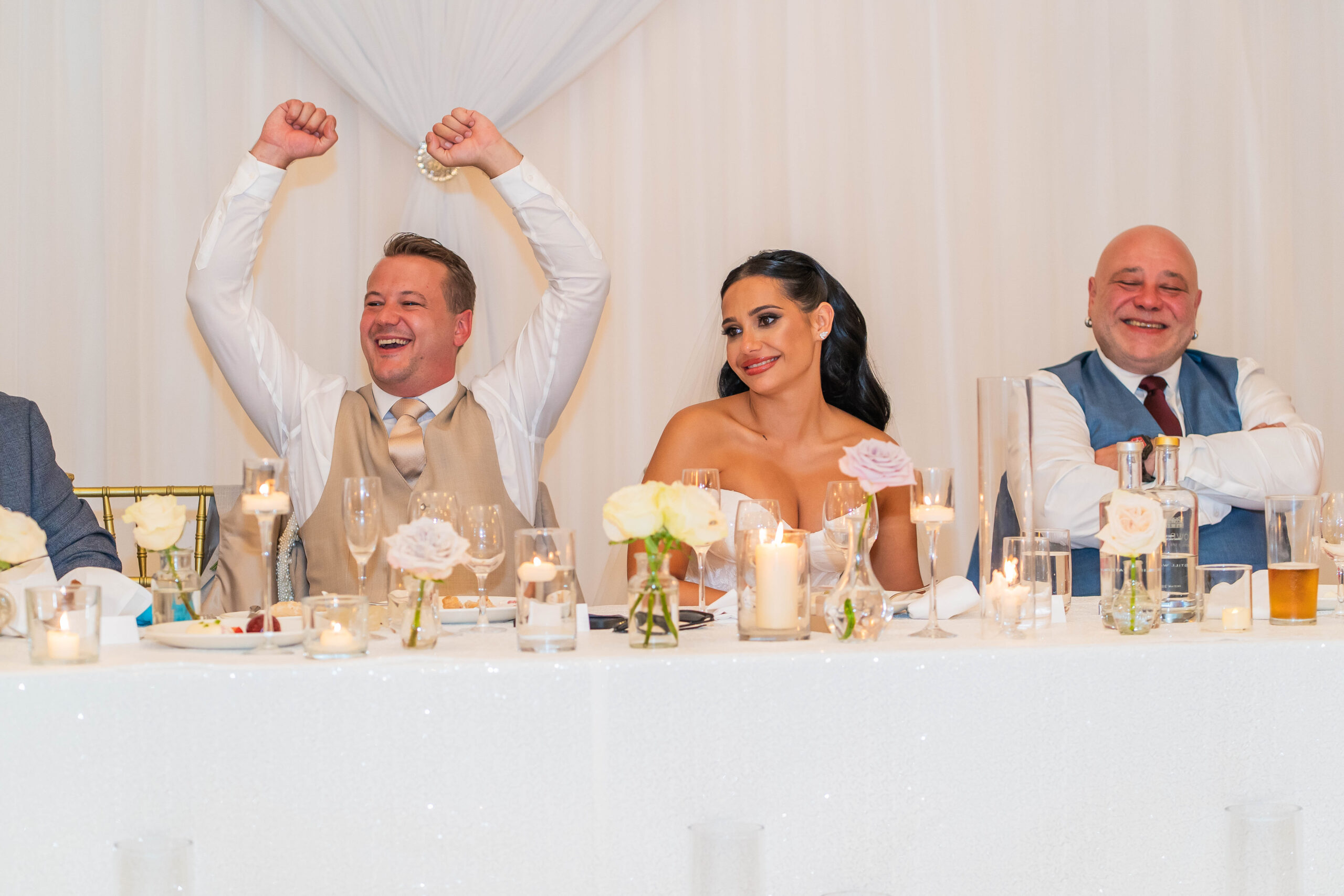 groom cheering with arms in the air as he listens to the speeches at the top table