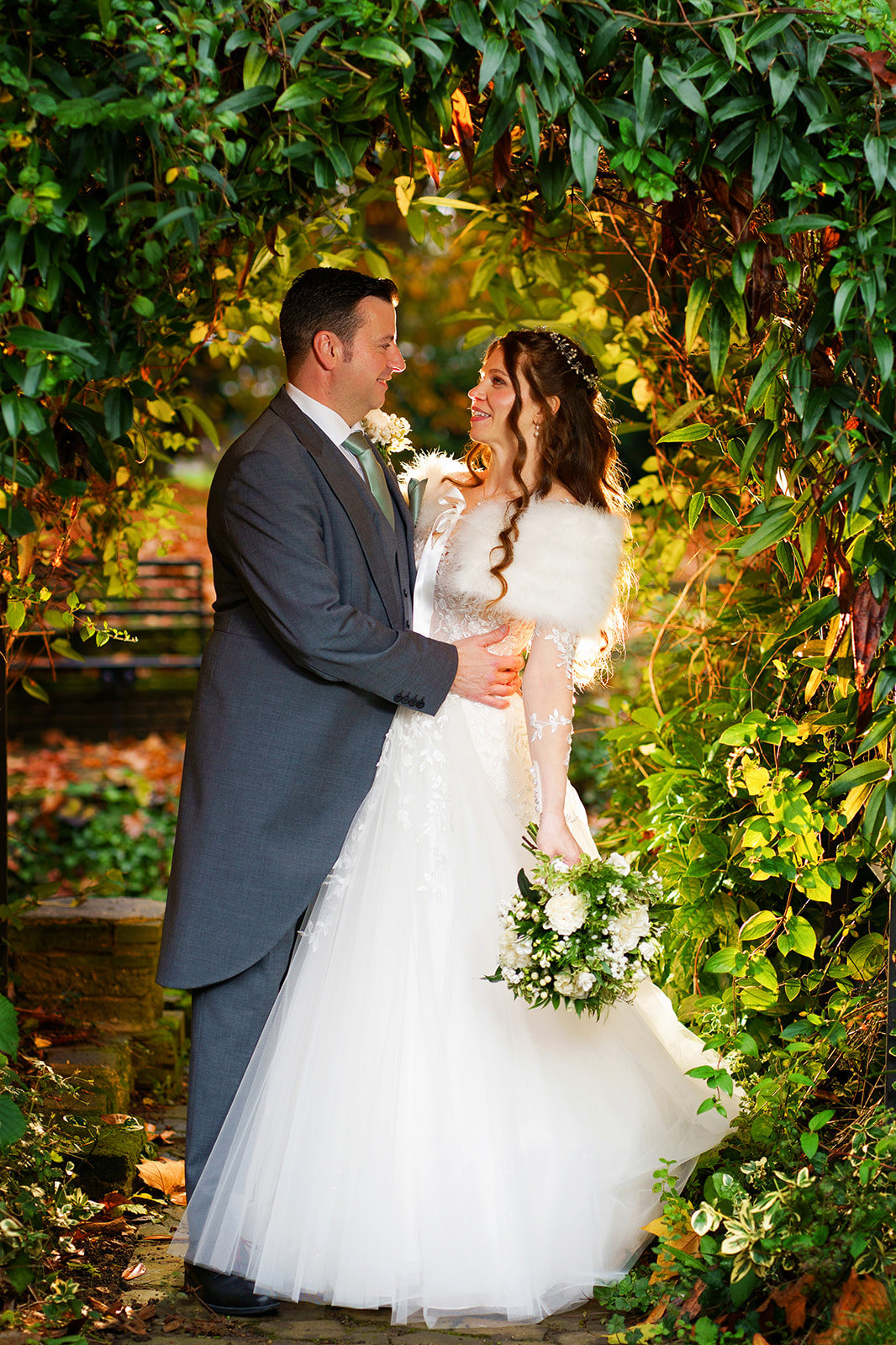 bride and groom stand under a stone archway surrounded by greenery.