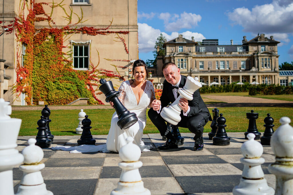 wedding at down hall - the bride and groom crouch by the outside chess board