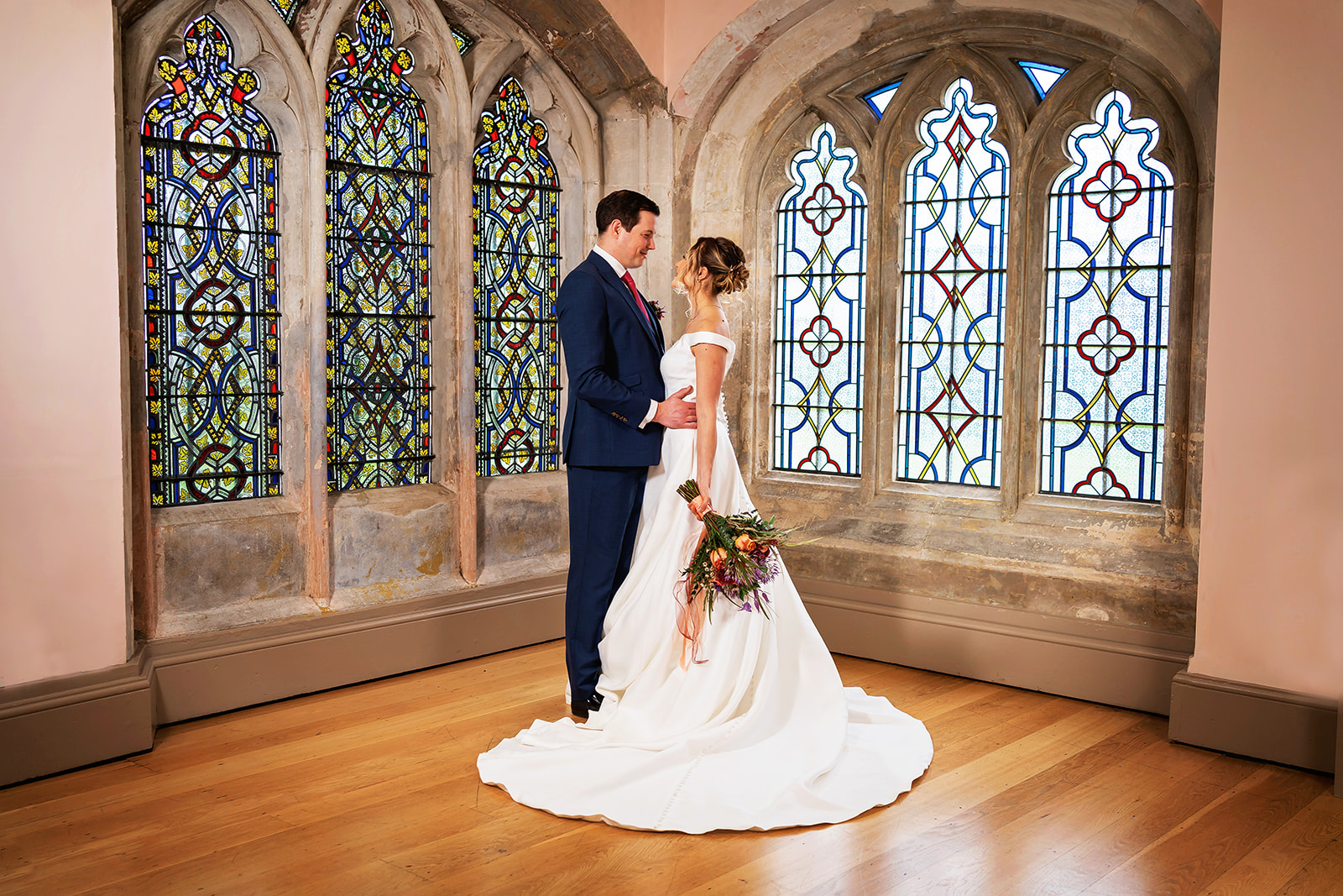 ware priory wedding photographer shoots bride and groom in a stone room with stained glass behind them