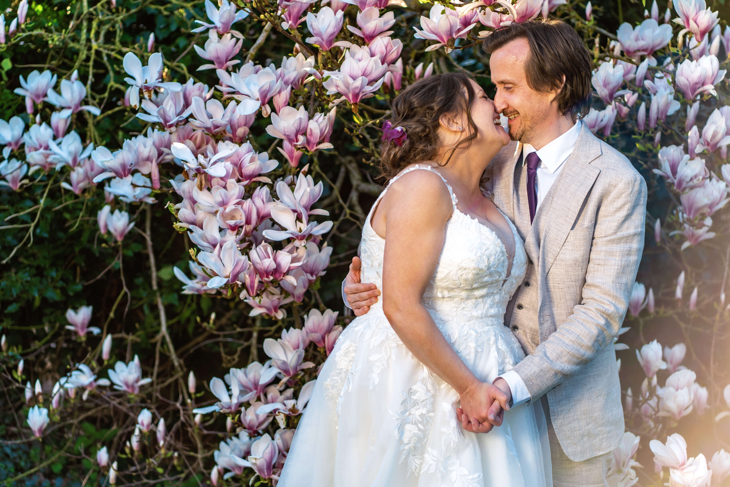 getting married later in life this bride and groom stand in front of pink blooming magnolia having a kiss