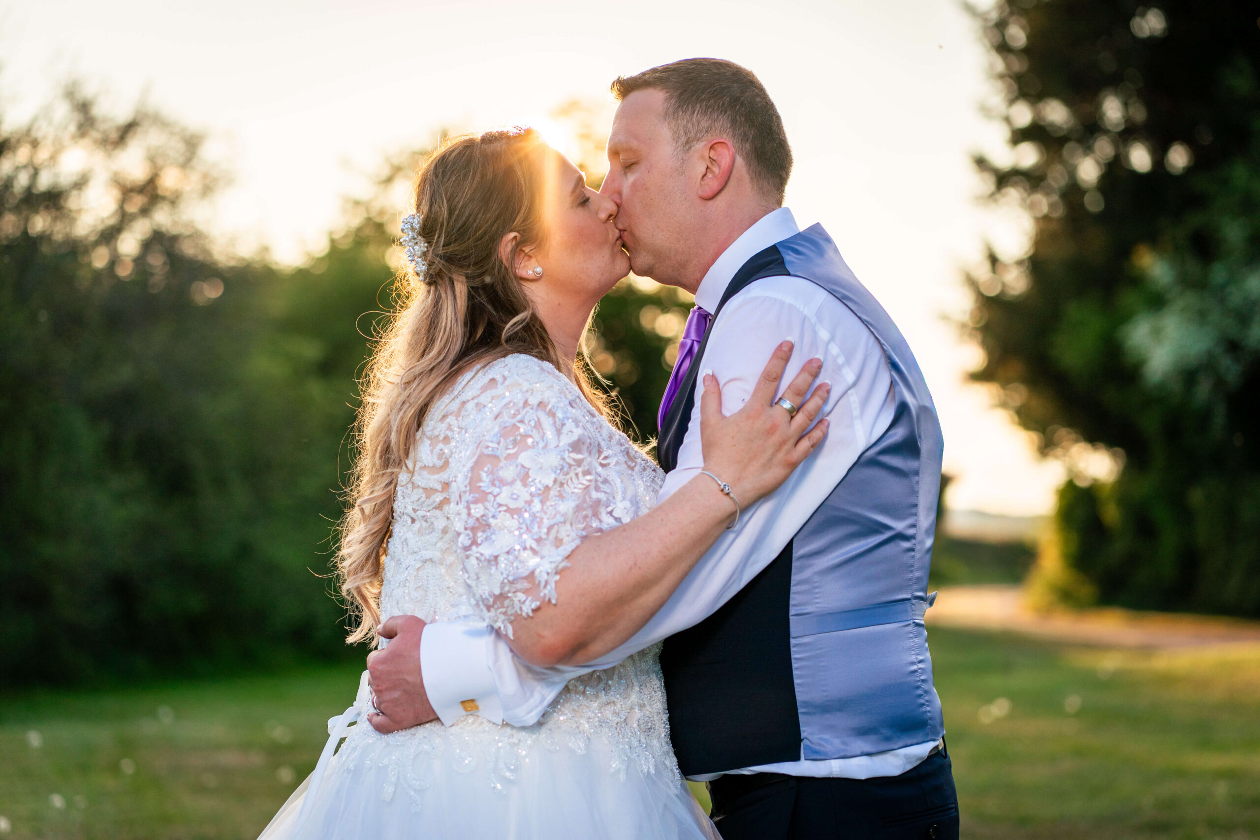 mature bride and groom kiss at sunset and the sun shines through the gaps